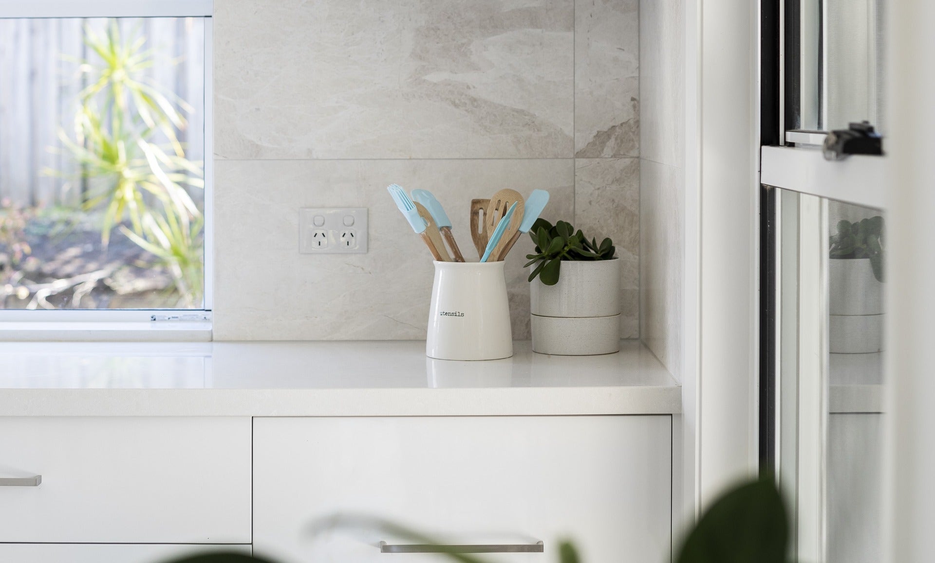 A stone-look porcelain tile on a kitchen splashback mimics the appearance of natural stone with a textured surface and subtle, varied color tones that resemble stone's natural veining and patterns.