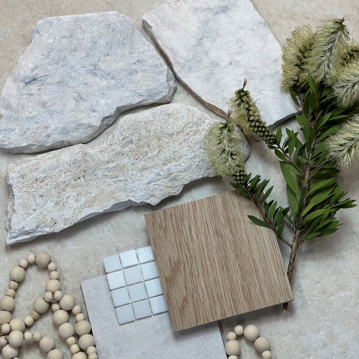 A minimalist Scandinavian flat lay featuring sleek, natural materials purchased from Amber. The composition includes neutral-toned porcelain tiles with a matte finish, a light oak wood sample, a sprig of greenery. The overall aesthetic is clean, calm, and timeless, highlighting the beauty of simplicity and natural elements. Perfect for creating a serene, scandinavian-inspired interior.