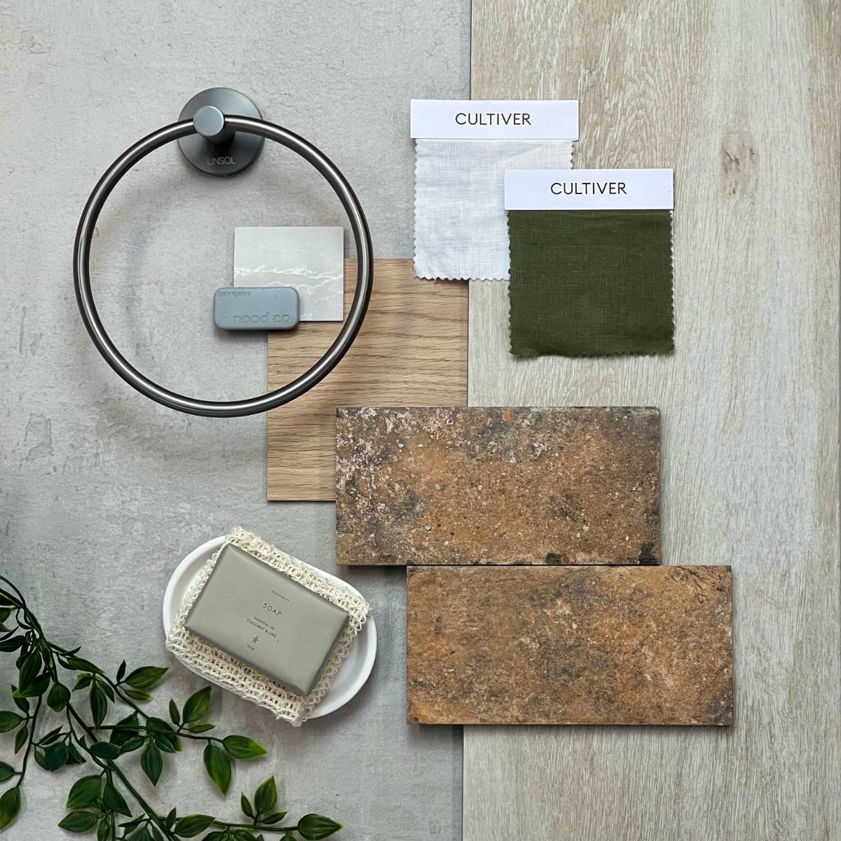 Flat lay of industrial-style materials purchased from Amber, featuring a mix of raw and textured finishes. The arrangement includes concrete-look tiles, matte black hardware, weathered wood samples, and brushed metal accents, all set against a neutral background. 